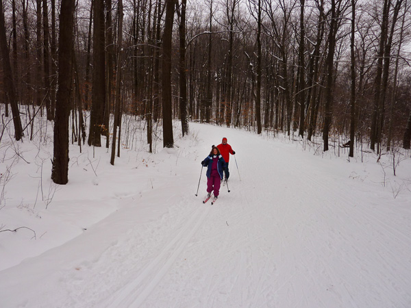 Jill Noble and her guide, Steve Plowk, with Jill in front. Normally, a team skis on a pre-conditioned set of ski tracks with the guide behind giving directions to the visually impaired person in front. In this picture, they are skiing through the woods.