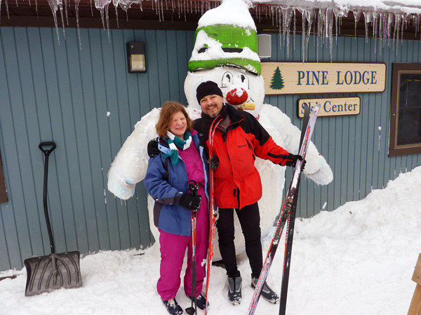 Jill Noble and Roger Meridith with cross country skis in hand standing in front of a giant snowman.